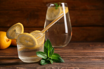 Glass and jug of fresh lemonade with mint on wooden background