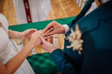 Fototapeta premium Close-up of groom placing a wedding ring on the bride’s finger during the ceremony, symbolizing love, unity, and commitment..