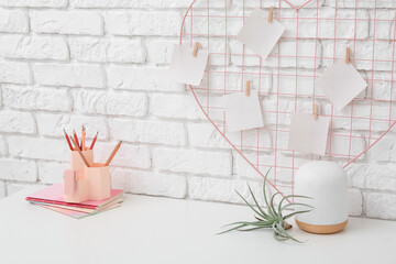 Modern workplace with moodboard, stationery and plant near white brick wall in office