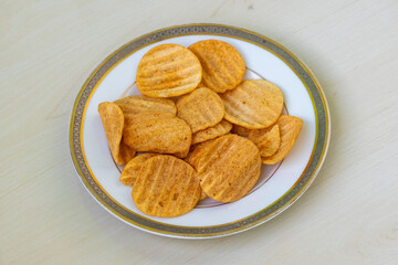 Crispy potato chips on a ceramic plate, resting on a light wooden surface. Delicious Bombay Sweets...