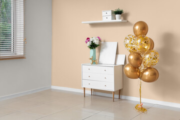 Beautiful golden air balloons with home decor and flowers on commode near beige wall at home