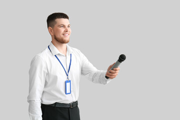 Male reporter with microphone and blank name tag taking interview on grey background