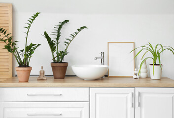 Chest of drawers with houseplants, sink and statuettes in light bathroom