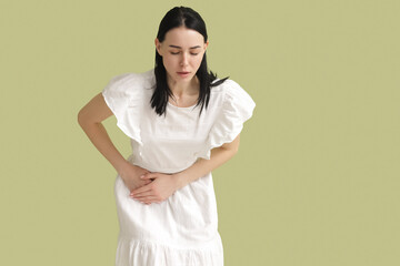 Young woman suffering from severe abdominal pain on green background