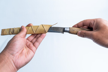 Close-up of a hand holding a traditional Flores knife with woven palm sheath, isolated on white background. Ideal for culture, tradition, craftsmanship, and ethnographic themes.