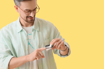 Young man with pulse oximeter on yellow background
