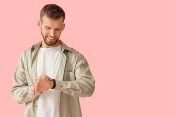 Young man with smartwatch checking his pulse on pink background