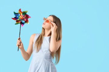 Young woman in sunglasses with toy windmill on blue background