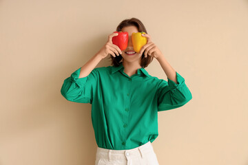 Beautiful young happy woman with fresh bell peppers on beige background. Diet concept