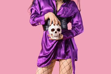 Beautiful young woman dressed as witch for Halloween with human skull on pink background, closeup
