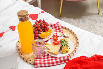 Tasty breakfast with juice on bed in room decorated for Valentine's Day, closeup