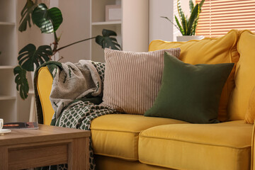 Comfortable yellow sofa with pillows in room, closeup
