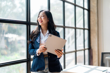 Businesswoman holding tablet and looking out window in modern office