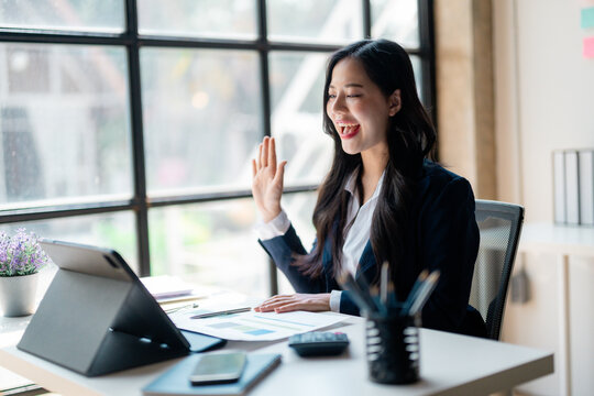 Asian businesswoman waving during video call on tablet in office