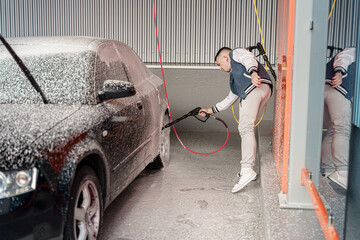 Man washing a car with foam solution in a modern car wash facility during daylight hours