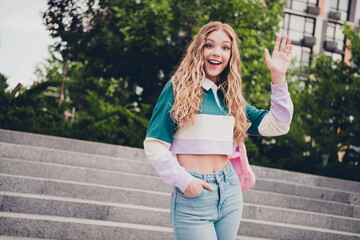 Portrait of pretty young girl rucksack arm wave hi you wear top city center outdoors