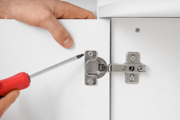 Male carpenter tightening screw in cupboard hinge with screwdriver, closeup