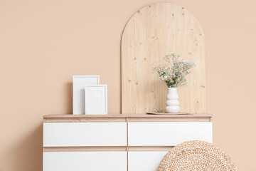 Chest of drawers with decor and gypsophila flowers in vase near beige wall in room