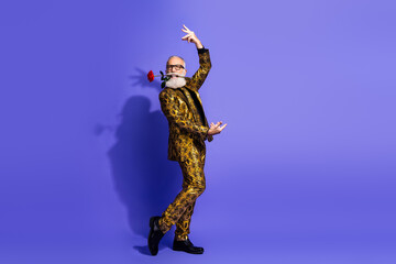 Stylish senior gentleman in a golden suit performs a playful dance holding a rose against a vibrant...