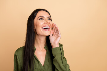 Young attractive businesswoman in green blouse smiling and gesturing against a beige background