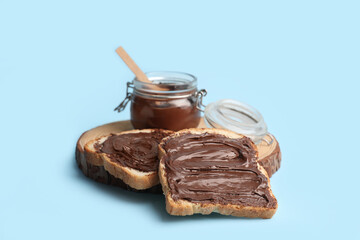 Wooden board of toasts with sweet chocolate spread on blue background
