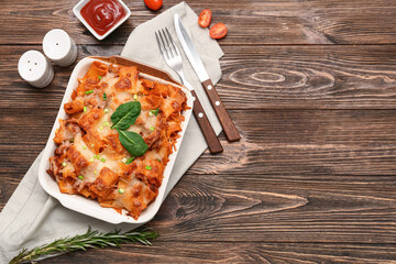 Baking dish with tasty pasta, cut green onion, spinach leaves, rosemary and bowl of ketchup on wooden background