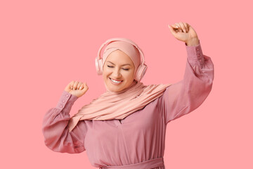 Beautiful Muslim woman in hijab with modern headphones on pink background