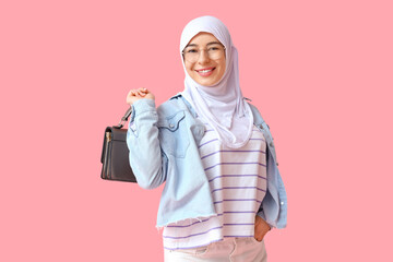 Beautiful young Muslim woman in hijab with stylish handbag on pink background