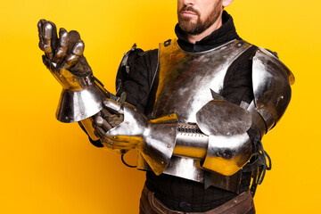 Man in medieval armor standing against a bright yellow solid background