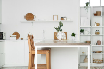 Interior of stylish kitchen with white counters, table and shelving unit
