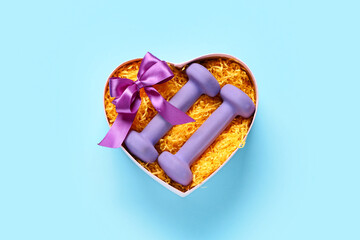 Gift box with purple dumbbells and bow on blue background