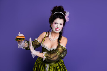 Elegant young woman in historic green dress rejecting a modern burger on a purple background