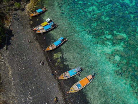 Aerial view of colorful boats moored along rocky shoreline with clear turquoise water, creating serene coastal scene
