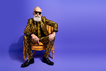 Stylish elderly gentleman in a vibrant patterned suit sitting confidently on a decorative chair