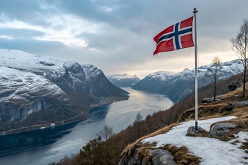 The Norwegian flag flying on a fjord cliff with snow in the background