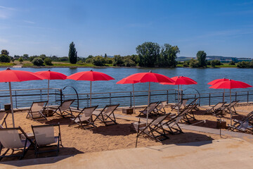 Sunny beach area with red umbrellas and lounge chairs by the river Rhine in summer