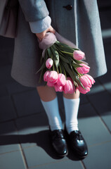 Photo des jambes d'une collégienne adolescente tenant un bouquet de tulipes roses pour la fête des mères, portant un manteau gris, des chaussettes blanches et des mocassins noirs d'uniforme de collège