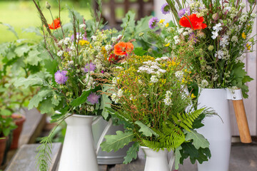 Bouquets of wild summer flowers in white jugs placed on wooden bench, celebrating summer solstice, beauty of nature. Traditional floral gathering ritual in a rustic countryside setting. Ligo. Latvia