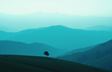 Misty mountains in teal tones, lone tree on grassy hill.