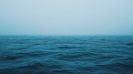 Obraz premium Ocean water with waves under a hazy sky creating a serene atmosphere.