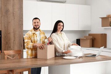 Fototapeta premium Happy young couple packing dishes in kitchen on moving day