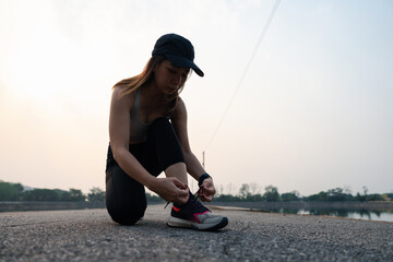 A woman ties her shoelaces while preparing to run on an empty road, showcasing determination and...