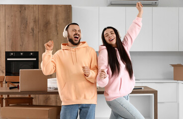 Happy young couple with headphones dancing in kitchen on moving day
