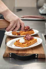 Chef pouring sauce on cooked waffle with brisket and cheese