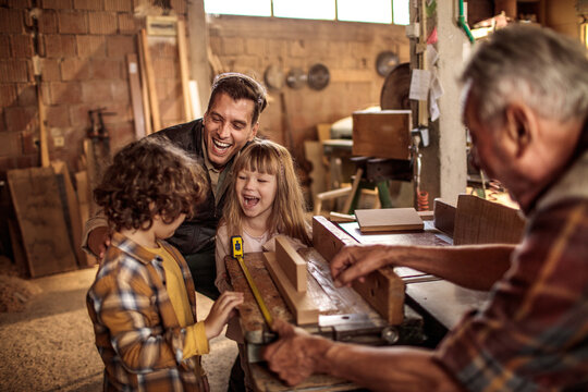 Grandfather teaching woodworking to grandkids with father in family workshop