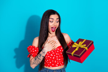 Excited young woman delightedly holding a gift box adorned with ribbon with a vibrant blue...