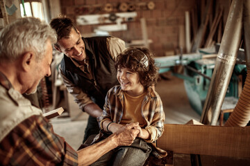 Happy grandfather teaching grandson carpentry with father in workshop