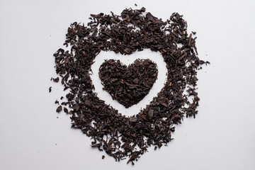 Black tea. A pile of tea leaves is laid out in the shape of a heart. The leaves are scattered around the center of the heart, creating a beautiful and unique design