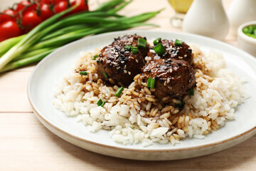 Delicious rice with meatballs, sauce and green onions on white wooden table, closeup
