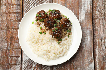 Delicious rice with meatballs, sauce and green onions on wooden table, top view